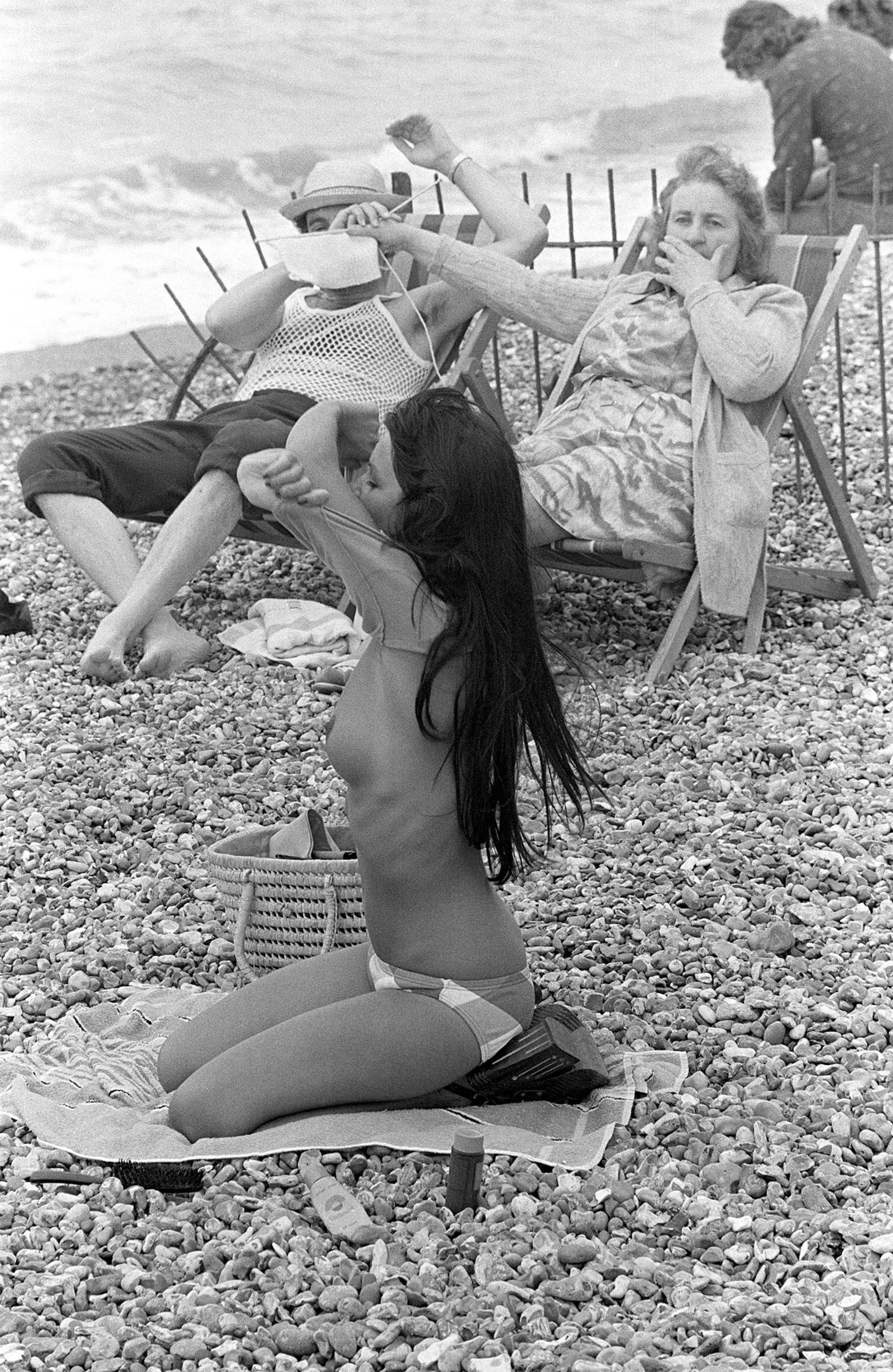 Woman covering man's eyes with her knitting at sight of young woman taking off her top on the beach in France, 1974 posted by maxwe11d